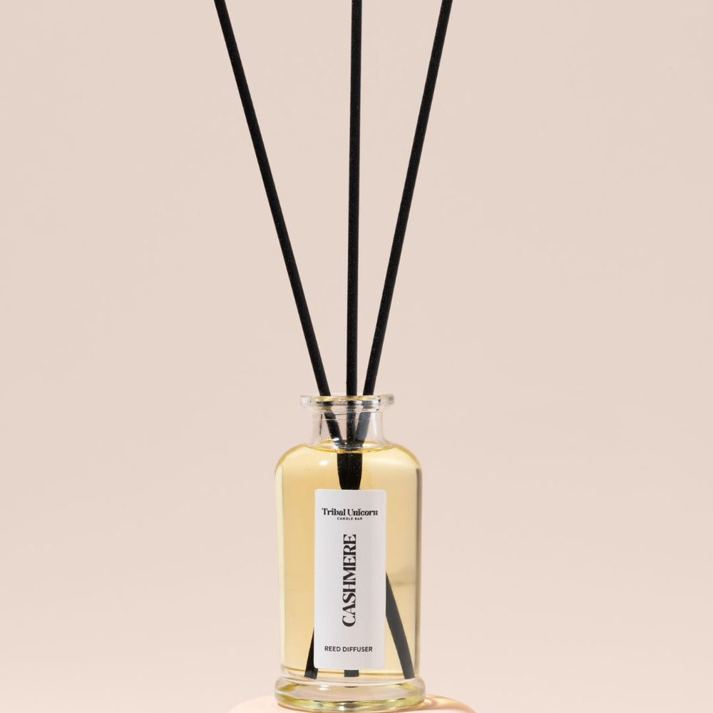 Reed diffuser with black reeds in a clear bottle on a beige background