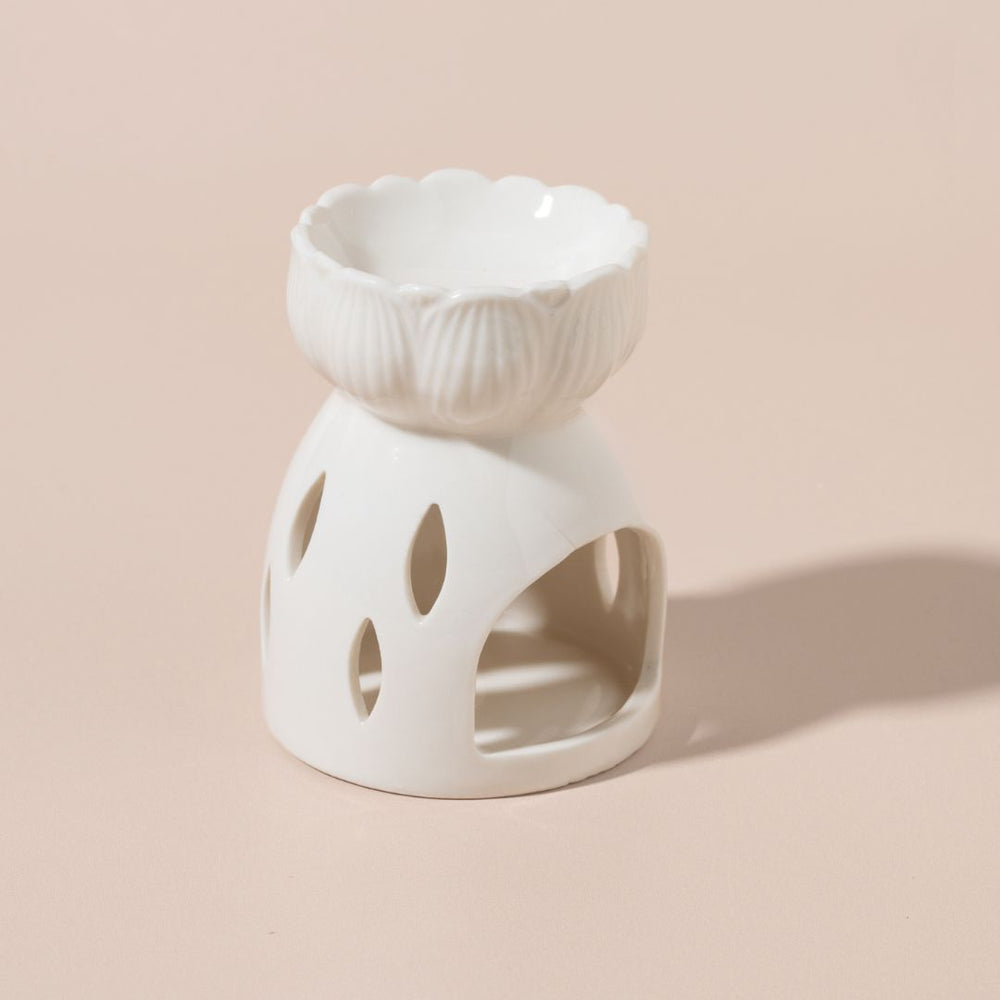 White ceramic oil burner with decorative design on a beige background