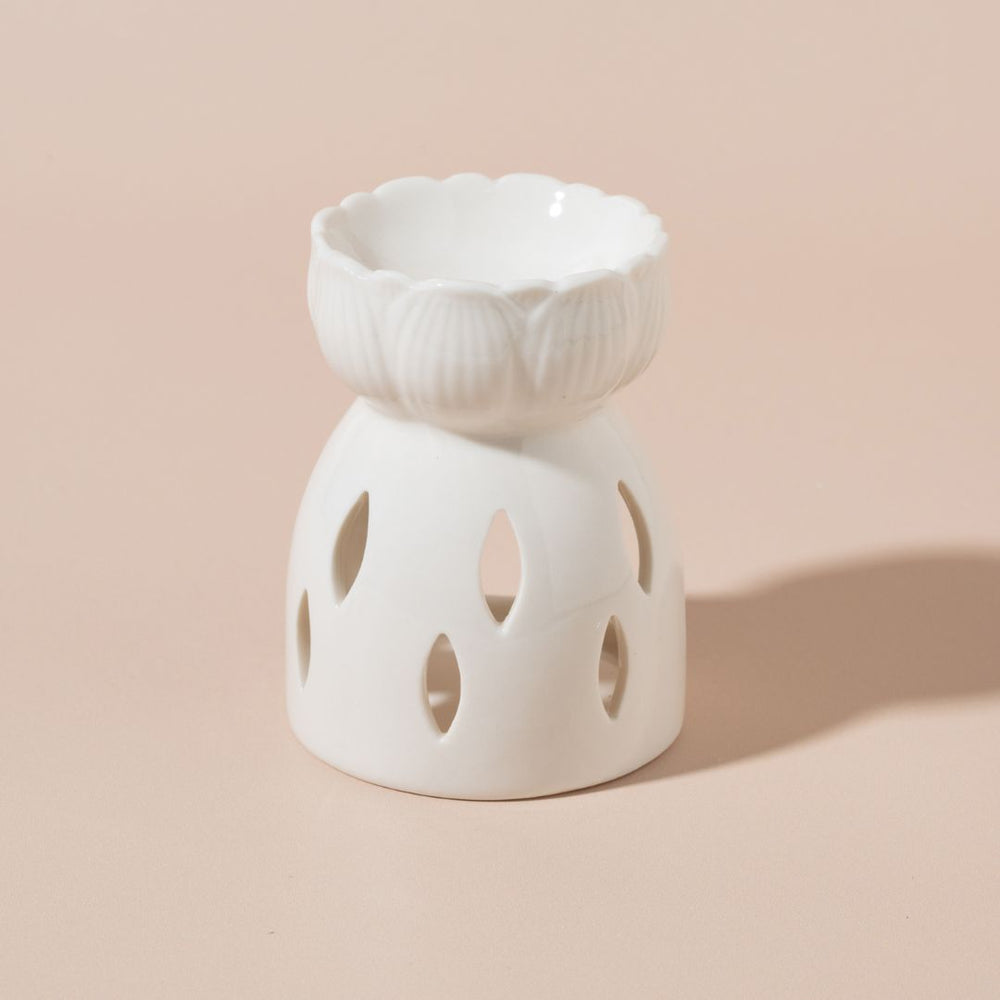 
                  
                    White ceramic oil burner with decorative top on a beige background
                  
                