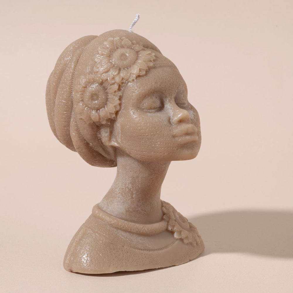 Candle bust of a woman's head with floral headpiece on a beige background