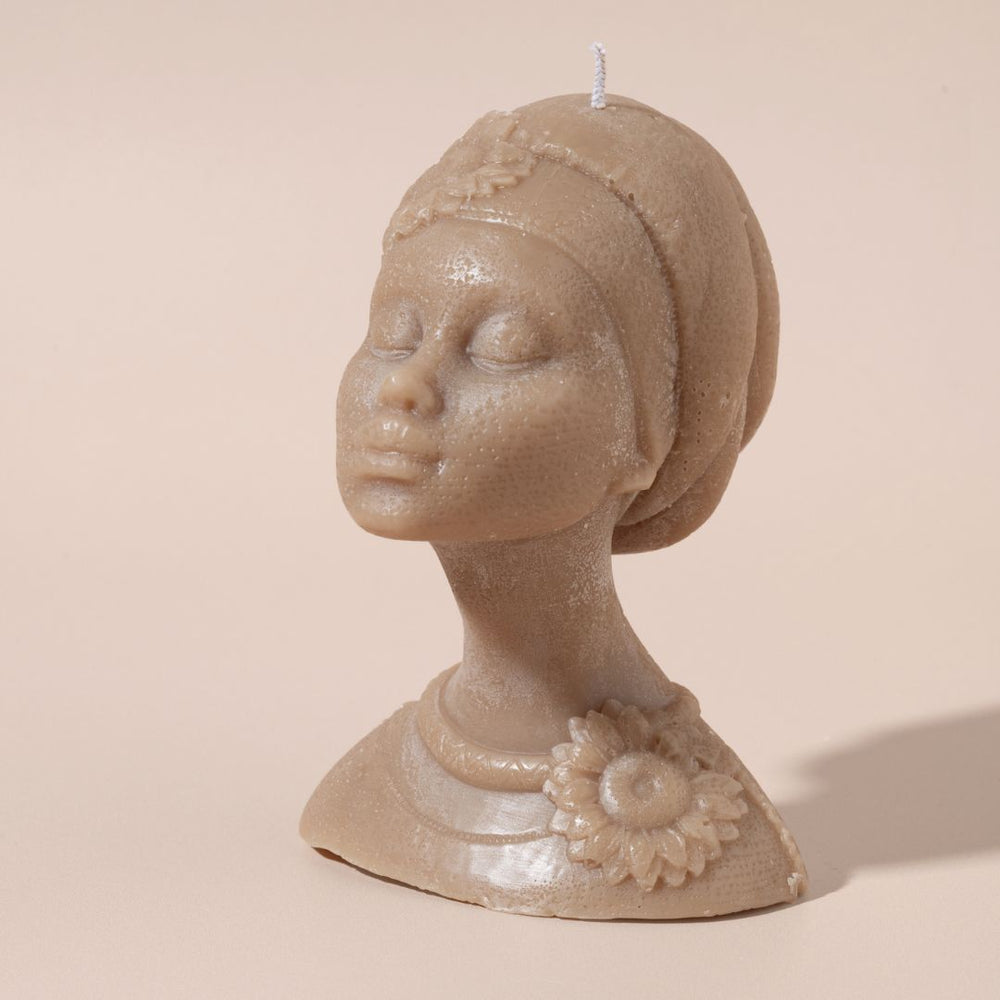 
                  
                    Candle shaped like a woman's head with a flower detail on a beige background
                  
                