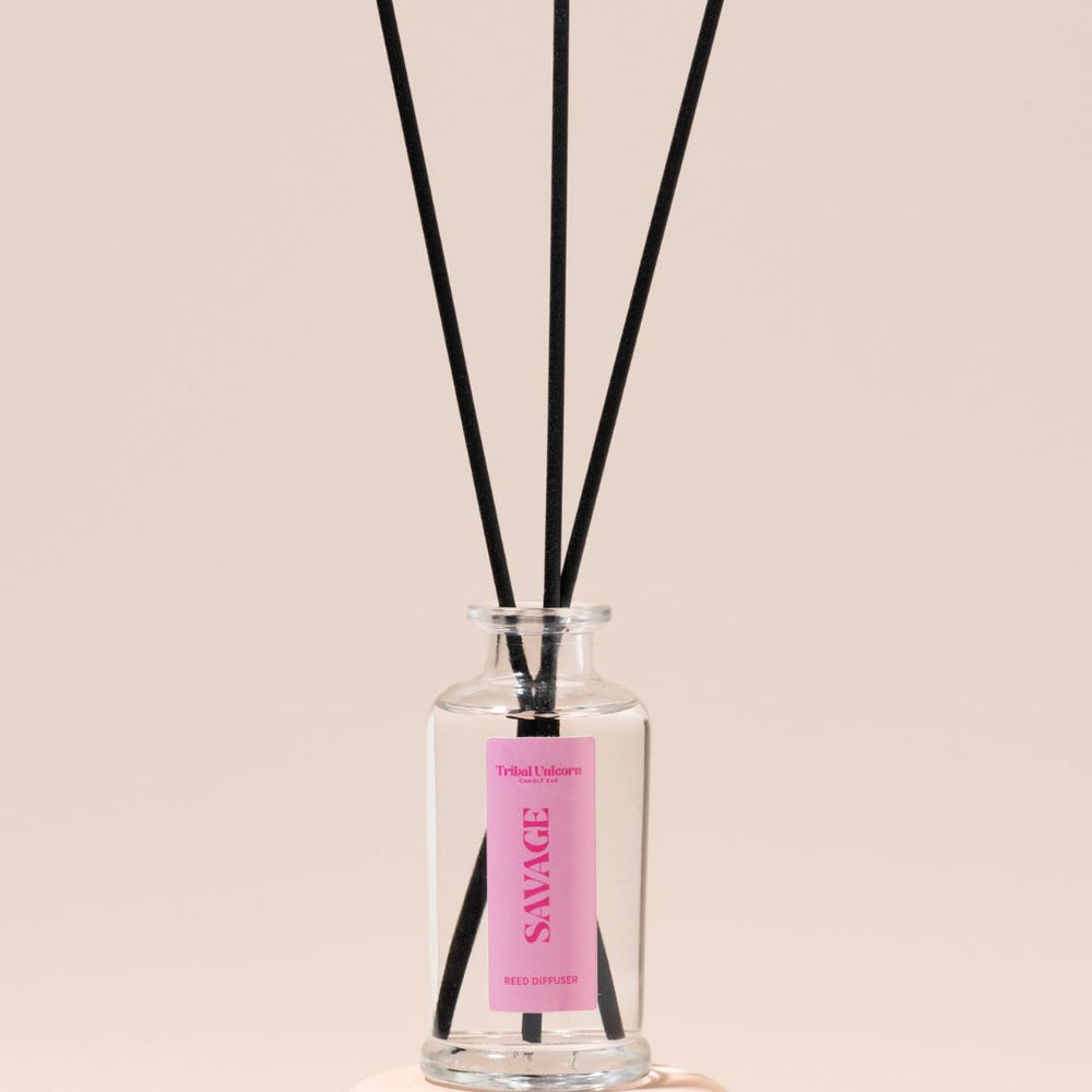 Reed diffuser with black reeds and a pink label on a beige background