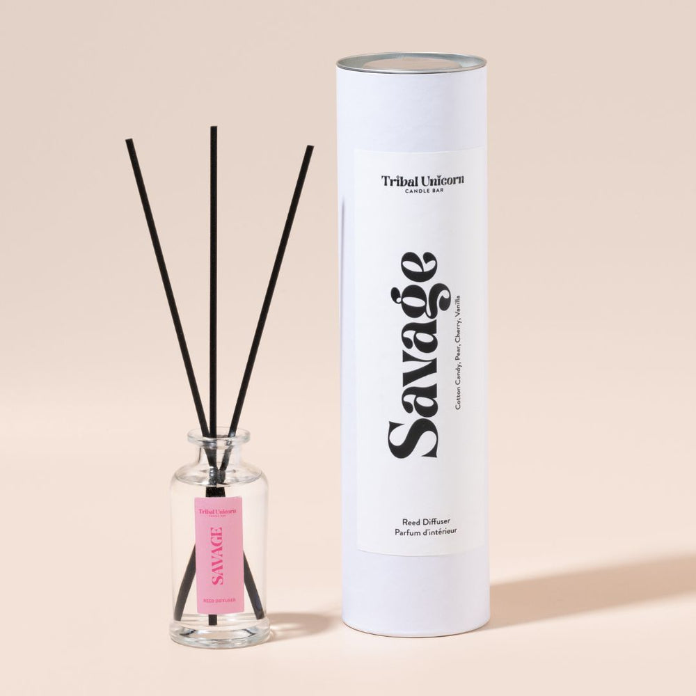 Reed diffuser with black reeds and a pink label on a beige background