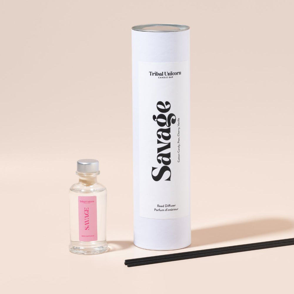 
                  
                    Reed diffuser bottle and packaging with pink 'Savage' branding on a beige background
                  
                